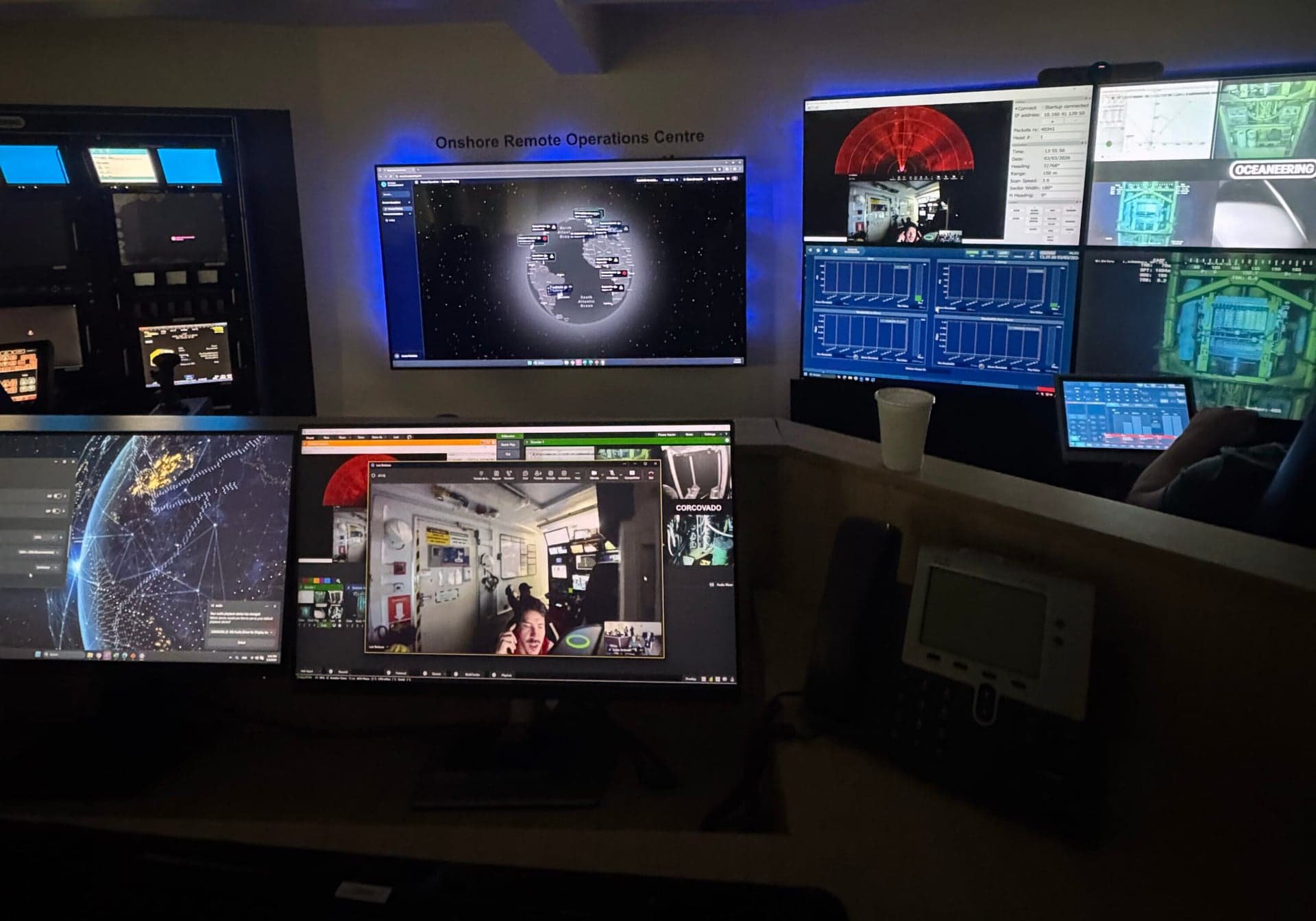 An ROV technician at an onshore remote operations center monitors screens displaying live feed from a remotely operated vehicle working on an offshore drilling rig.